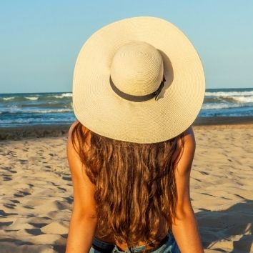 Dame met zonnehoed en lange haarlokken op haar rug op het strand nabij de zee